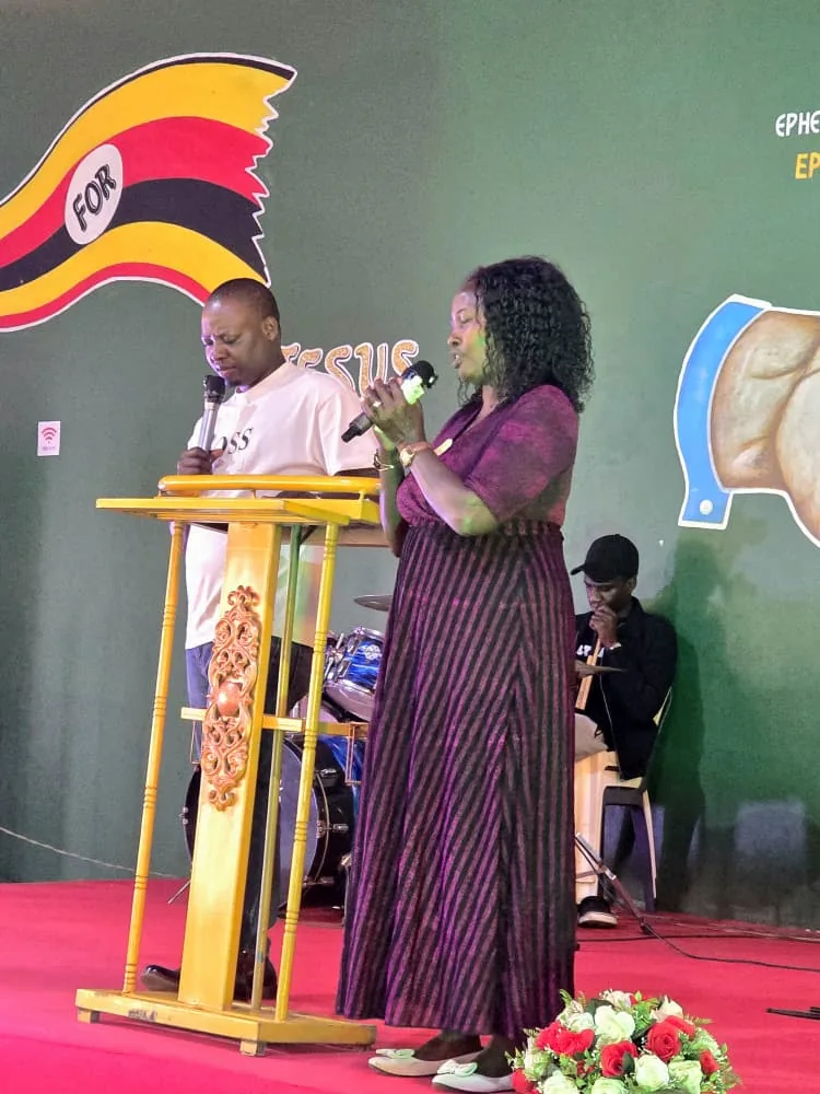 A woman speaking from the platform beside the Uganda flag